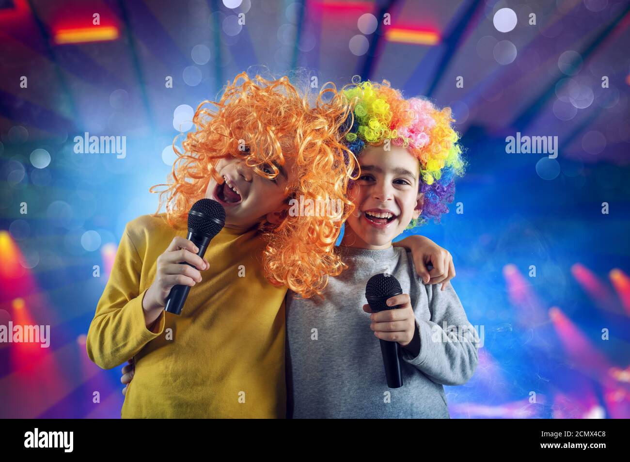 Zwei Kinder singen ein Lied mit Mikrofon und lustige Perücke Stockfoto