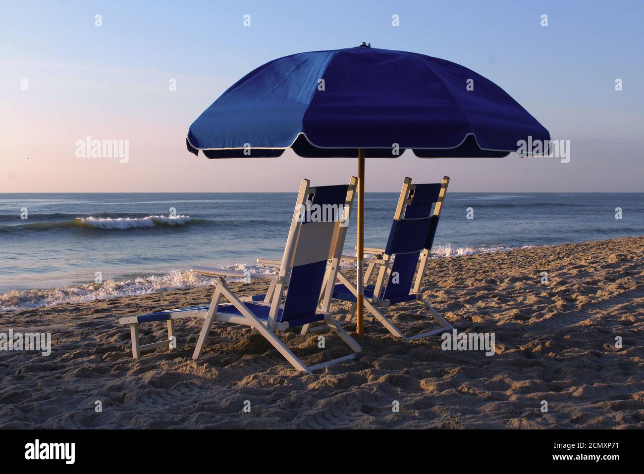 Liegestühle unter einem Sonnenschirm am Strand bei Sonnenaufgang. Stockfoto