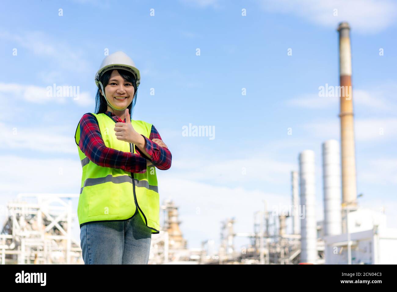 Asiatische Frau Ingenieur Arm gekreuzt und Daumen nach oben mit zuversichtlich freuen uns auf die Zukunft mit Ölraffinerie Fabrik im Hintergrund. Stockfoto