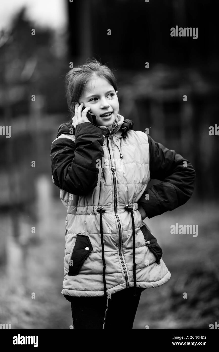 Kleines Mädchen im Gespräch auf dem Handy stehend auf der Straße. Schwarzweiß-Fotografie. Stockfoto
