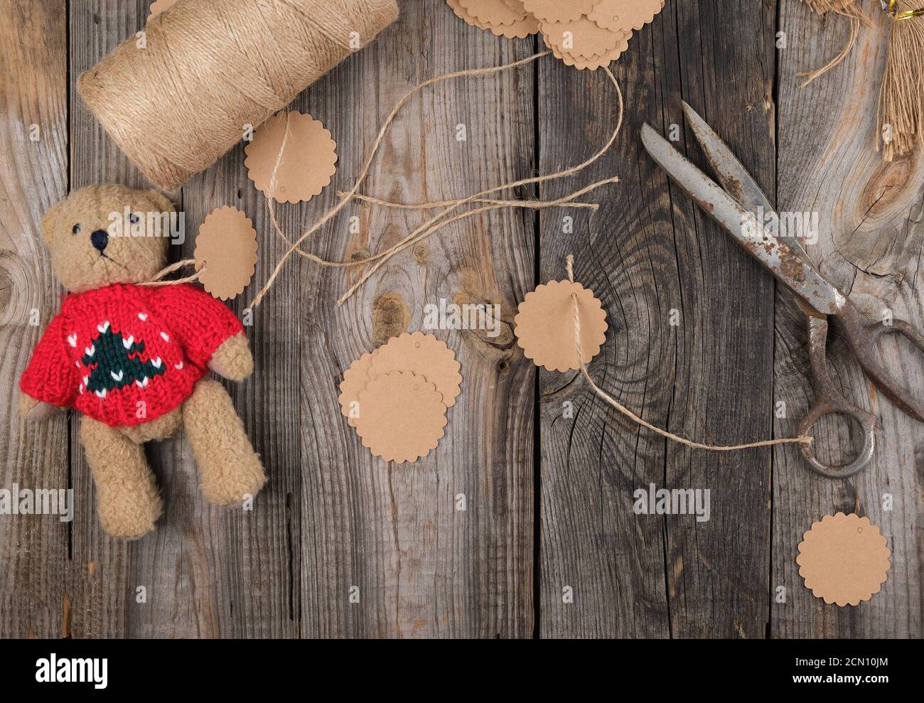 Spule aus braunem Seil, Papieranhänger und alter Schere auf grauem Holzhintergrund Stockfoto