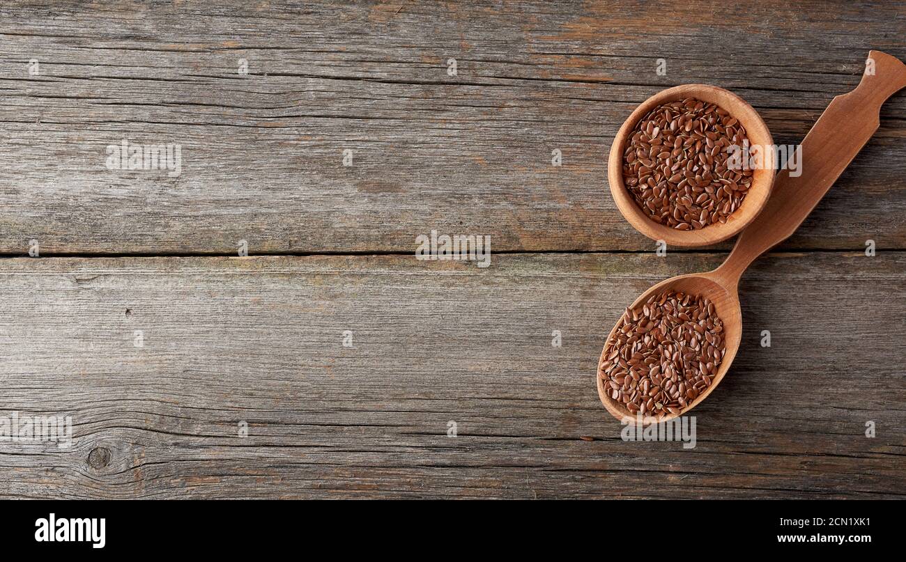 Trocknen Sie braune Leinsamen in einem braunen Holzlöffel auf Ein grauer Holztisch aus alten Brettern Stockfoto