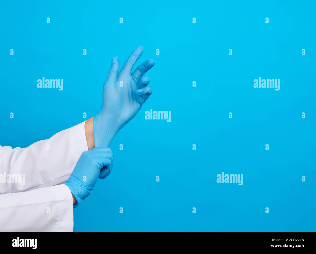 Ärztin im weißen Mantel zieht sich die Hände an Sterile medizinische Handschuhe aus blauem Latex an den Händen Stockfoto