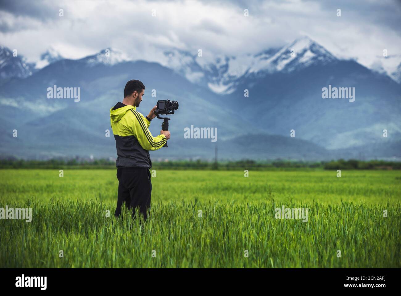 Mann, der die Kamera auf einem Stabilisator auf einem grünen Feld hält Malerischer Hintergrund Stockfoto