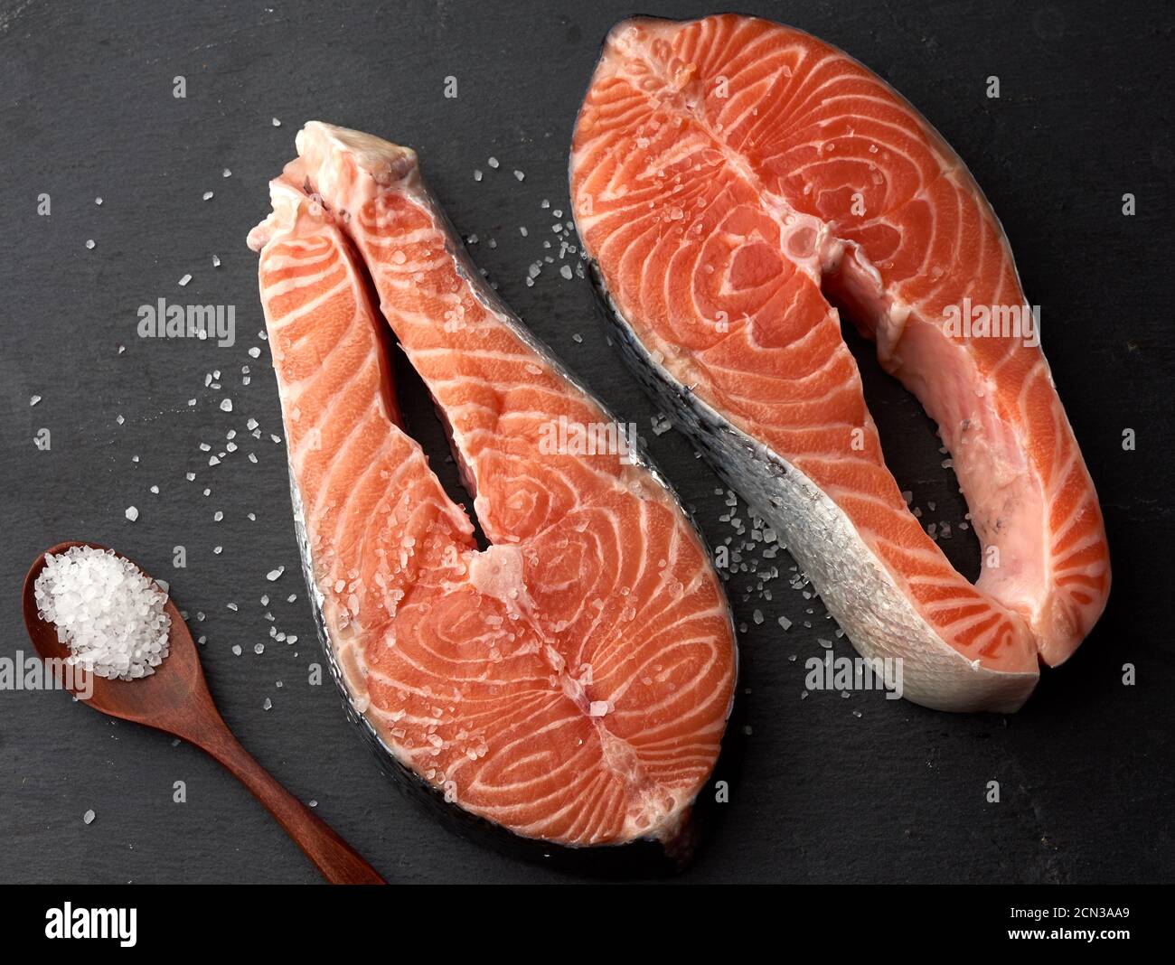 Zwei rohe Lachssteaks mit weißem Salz auf einem schwarzen Hintergrund Stockfoto