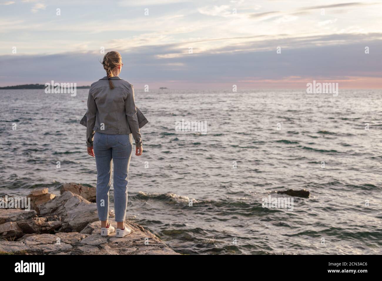 Rückansicht einer jungen Frau, die auf dem Steinpier steht Wandern am Meer Stockfoto