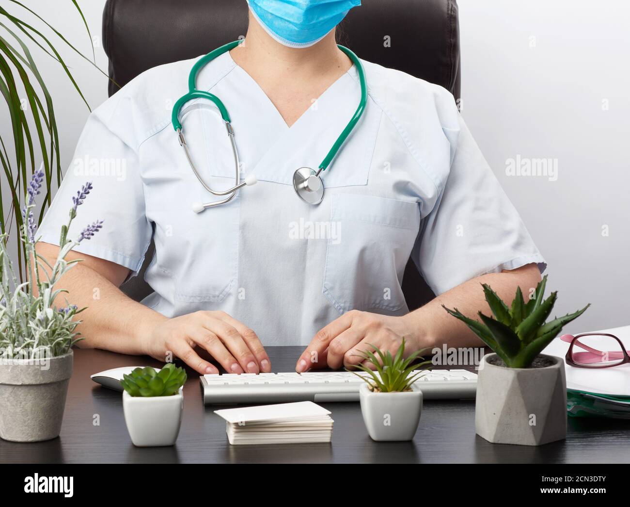 Doktor sitzt an einem weißen Tisch in blauer Uniform, Spezialist tippt auf einer Tastatur Stockfoto