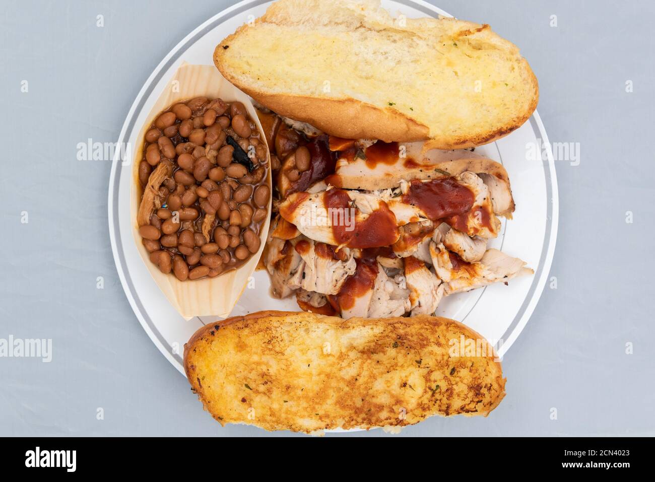 Blick von oben auf das BBQ-Essen mit geschnittenem Huhn, gebackenen Bohnen und Butter geröstetem Brot wird so lecker schmecken, wie es aussieht. Stockfoto