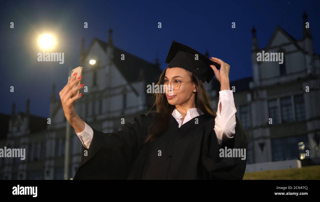 Absolvent Studentin Blick auf ihr selbst in ihrem Telefon und richtet sich ihr Outfit. Stockfoto