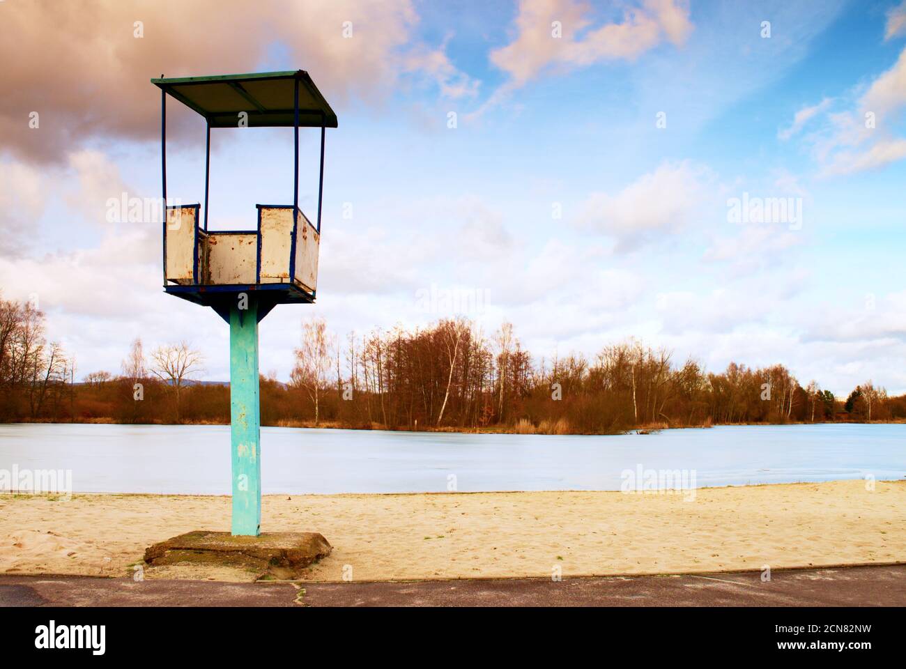 Alter weißer und rostiger Rettungsschwimmer-Turm aus Metall mit Stuhl am Strand. Gefrorener Wasserstand innerhalb von witer Stockfoto