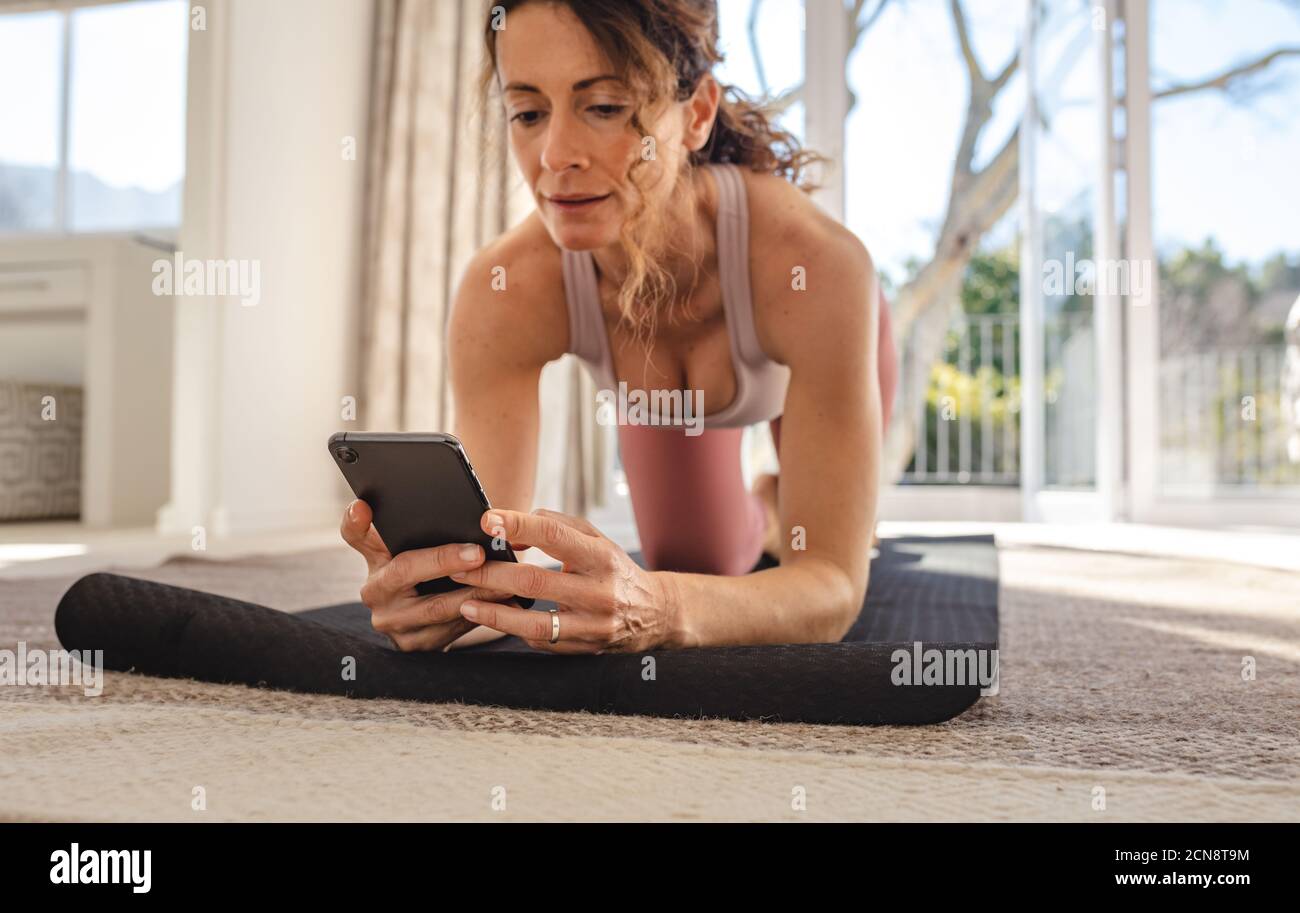 Frau schaut in das Telefon Online-Yoga-Unterricht während der Ausübung. Weiblich in Sportbekleidung mit ihrem Handy Workout-Tutorials online zu finden. Stockfoto