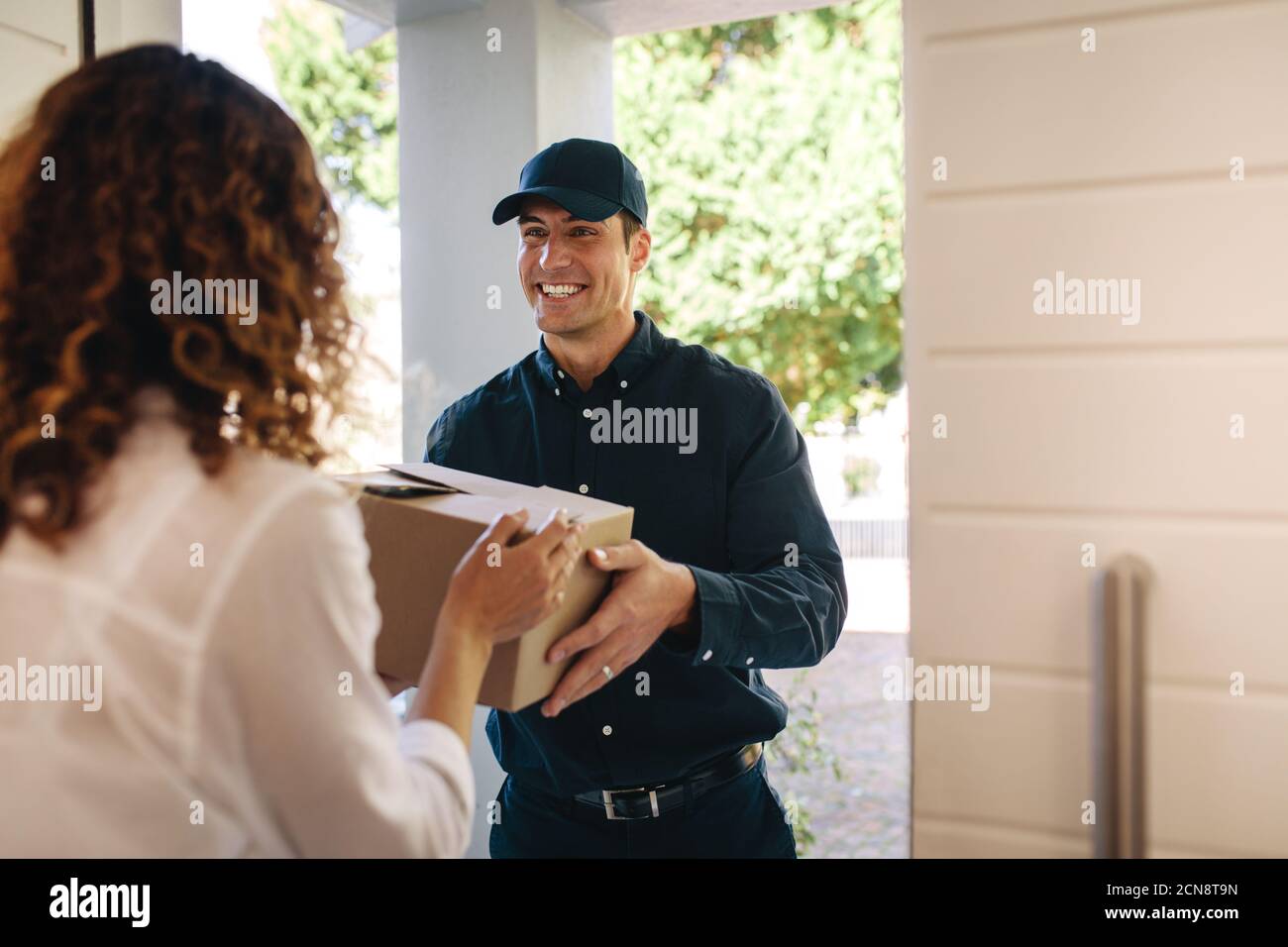 Lächelnder Delivery Mann, der eine Schachtel zu Hause an die Frau übergab. Kurierarbeiter liefert ein Paket an Frau. Stockfoto