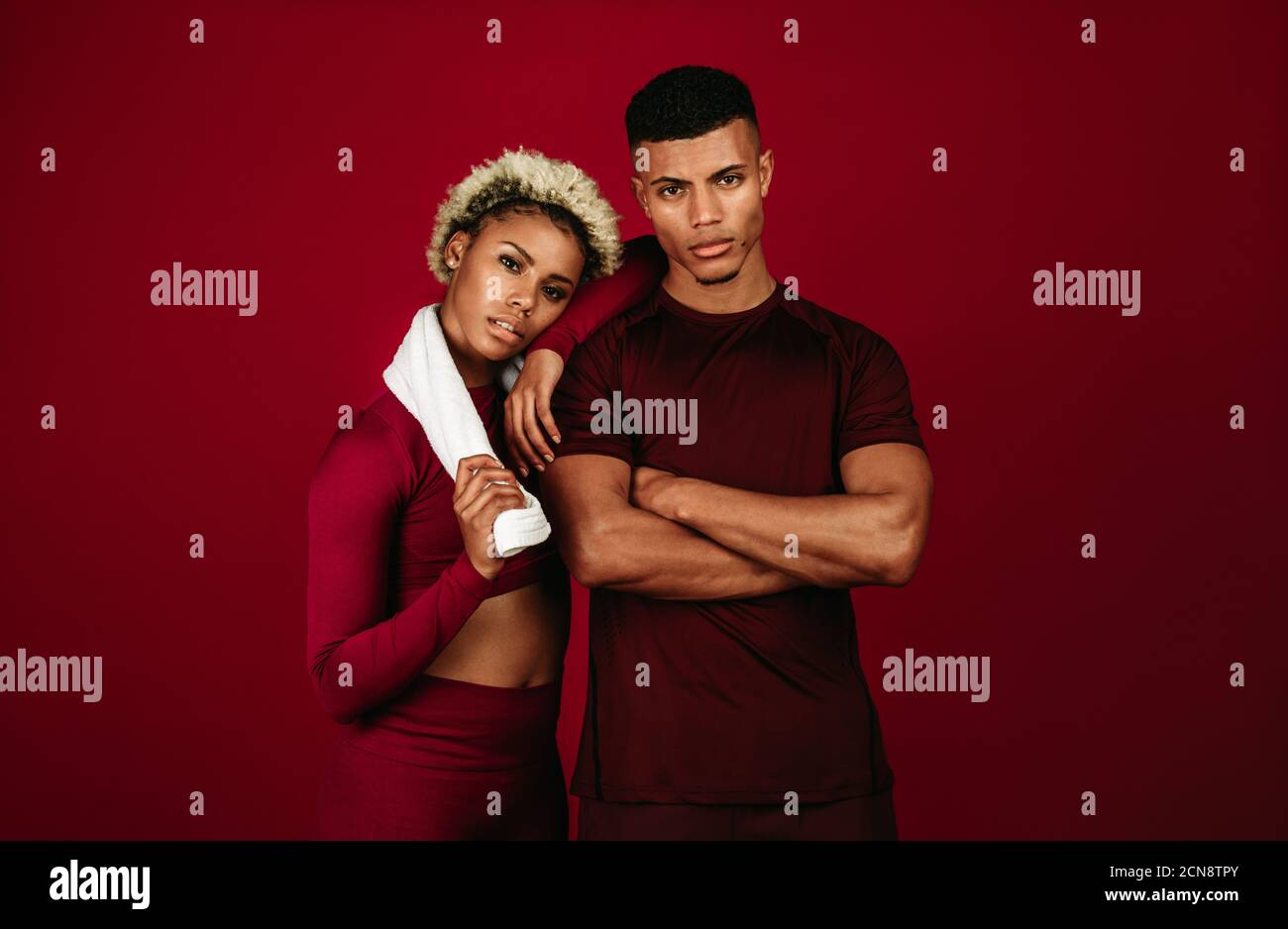 Muskulöses afroamerikanisches athletisches Paar, das zusammen auf kastanienbraunen Hintergrund steht. Fit Mann mit gekreuzten Armen stehen mit weiblichen Athleten. Stockfoto