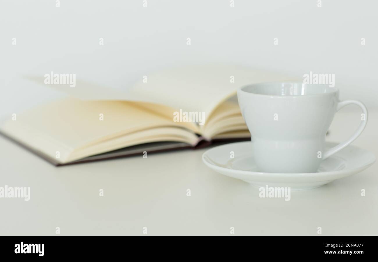 Öffnen Sie das Notizbuch mit leeren Seiten, die flach neben einer Kaffeetasse auf einer Untertasse liegen. Isoliert vor weißem Hintergrund. Ruhe Studie und Entspannung. Stockfoto