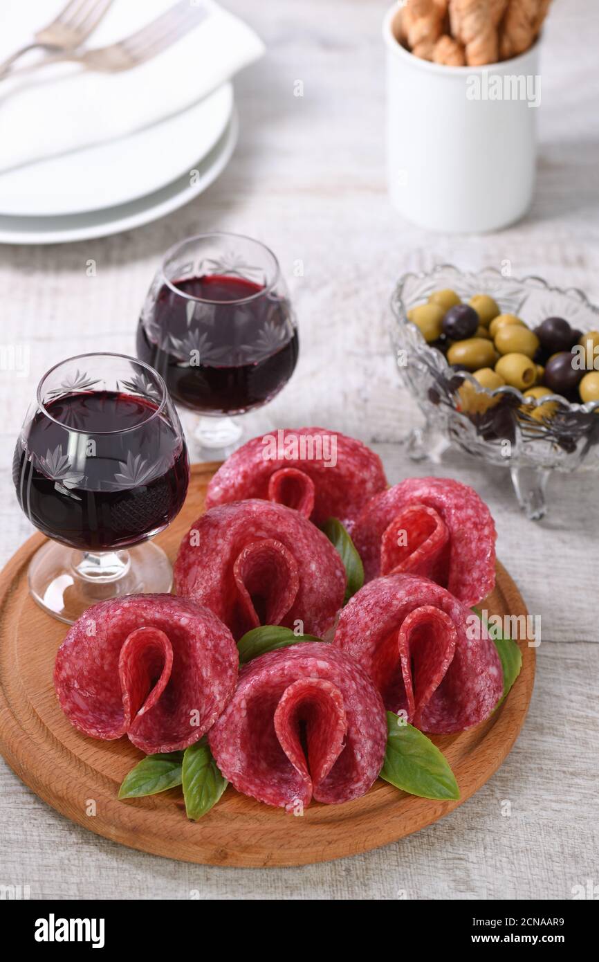 Leichte Mahlzeit Snack aus Salami gefaltet in Form einer Blume mit einem Glas Sherry auf einer Holzschale. Cl Stockfoto