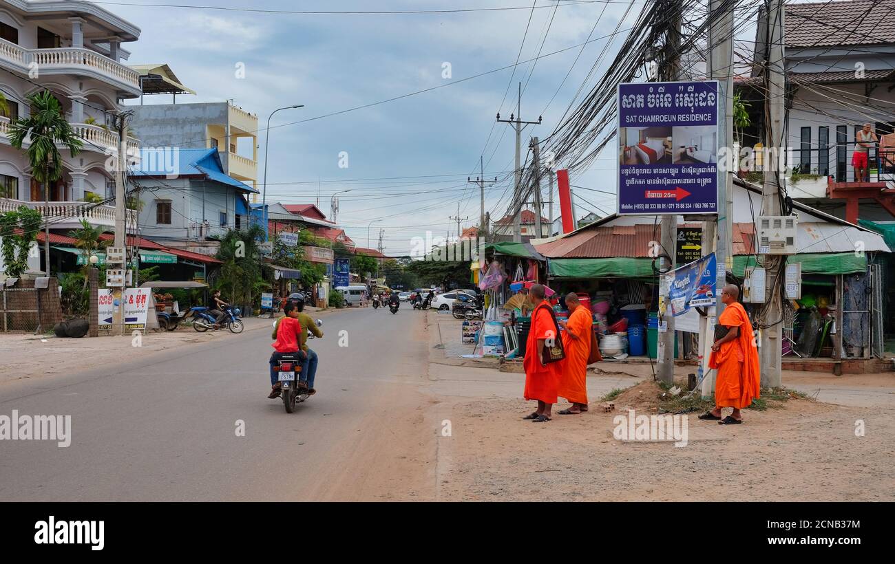 Kambodscha, Siem Reap 08/12/2018 mehrere buddhistische Mönche in orangefarbenen Kleidern stehen am Straßenrand, mehrere Motorroller fahren entlang der Straße Stockfoto