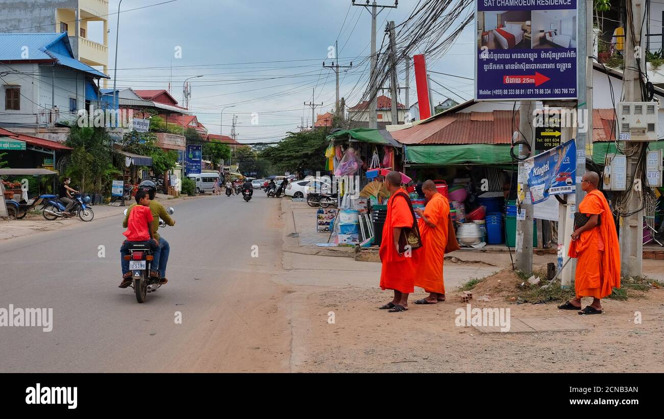 Kambodscha, Siem Reap 08/12/2018 mehrere buddhistische Mönche in orangefarbenen Kleidern stehen am Straßenrand, mehrere Motorroller fahren entlang der Straße Stockfoto