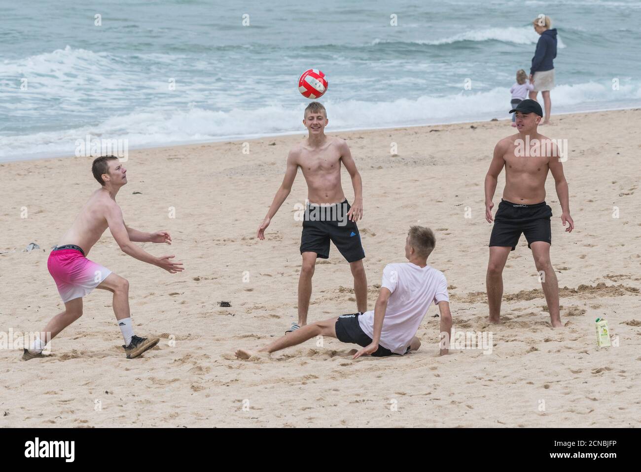 Eine Gruppe von Burschen, die in einem Kurzurlaub am Fistral Beach in Newquay in Cornwall mit einem Ball spielen. Stockfoto