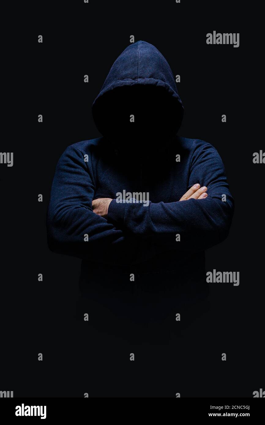 Mann in dunkelblauem Hoodie, Gesicht im Schatten versteckt, unkenntlich, gekreuzte Arme, allein im Dunkeln Stockfoto