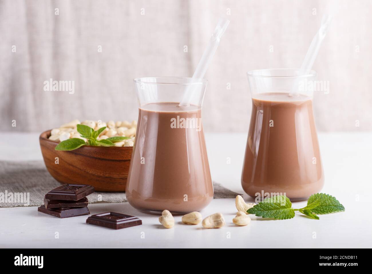 Bio-nicht-Milchkaschokolade-Milch in Glas und Holzplatte mit Cashewnüssen auf grauem Betongrund. Vegan gesundes Lebensmittelkonzept, Nahaufnahme Stockfoto