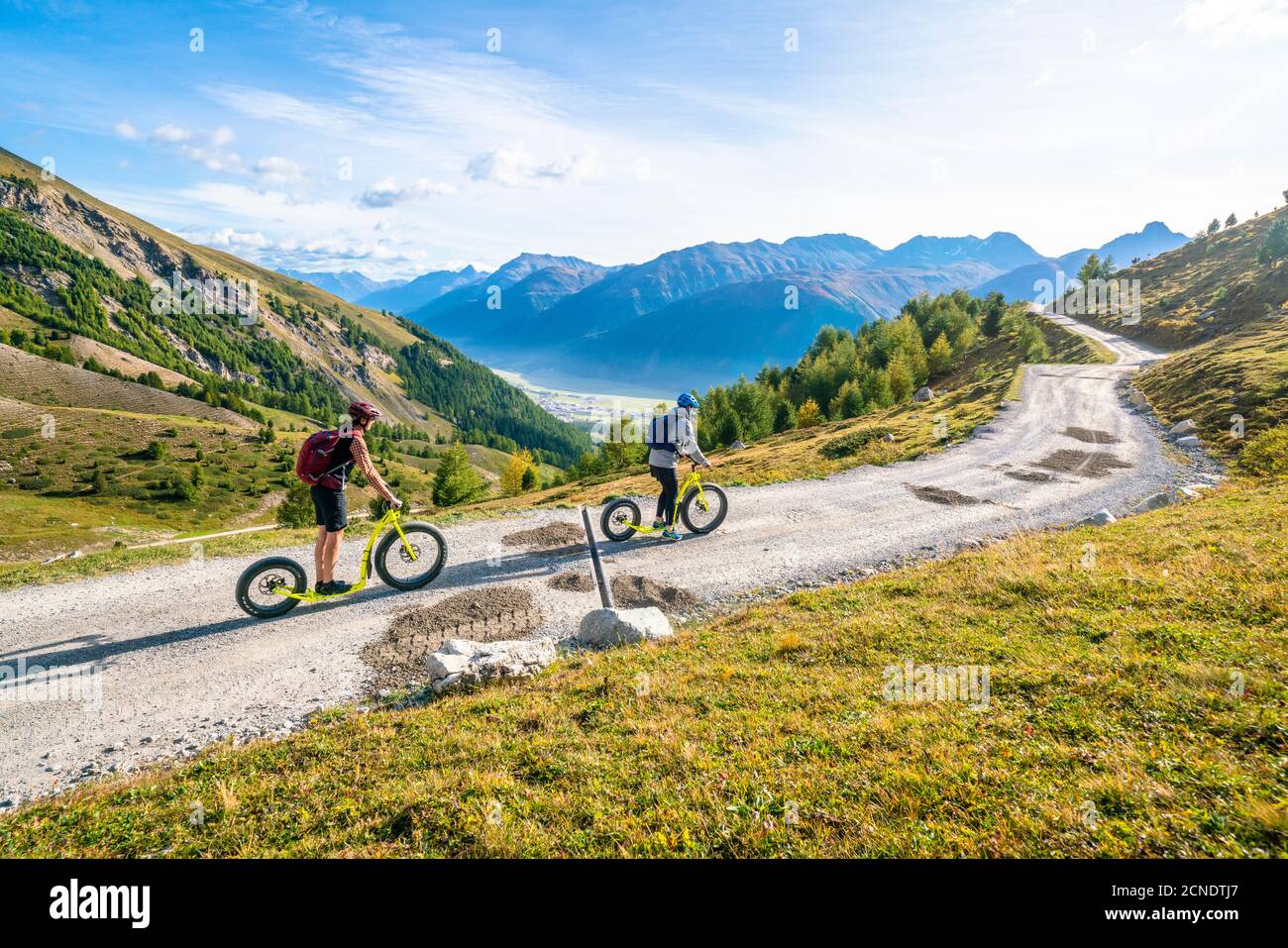 Zwei Leute haben Spaß beim Trottinet Scooter bergab von Bergstation Marguns nach Celerina, Engadin, Kanton Graubünden, Schweiz Stockfoto