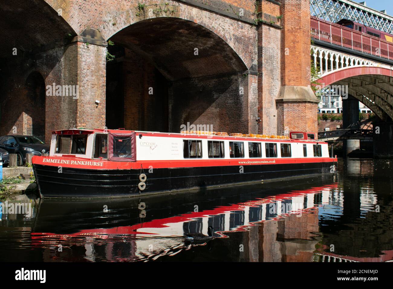 Die Emmeline Pankhurst Barge vertäute im Castlefield Basin, Manchester, Großbritannien, mit Kanalbrücke im Hintergrund und Reflexion im Wasser Stockfoto