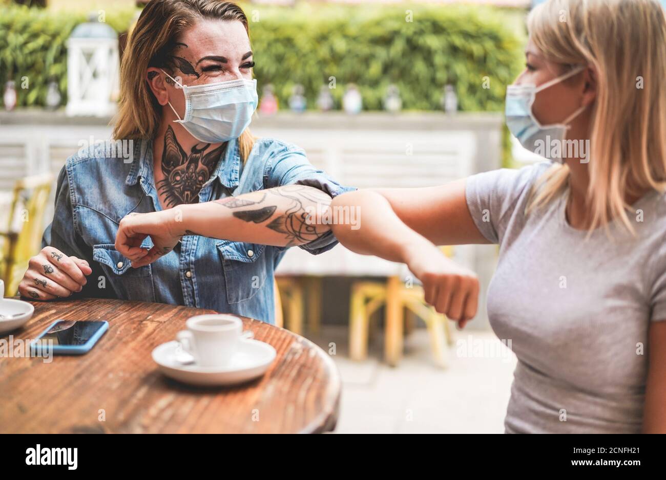 Junge Freundinnen stoßen ihre Ellbogen, anstatt mit zu grüßen Eine Umarmung - Vermeiden Sie die Ausbreitung von Coronavirus tragen schützende Masken - Soziale Distanz Konz Stockfoto