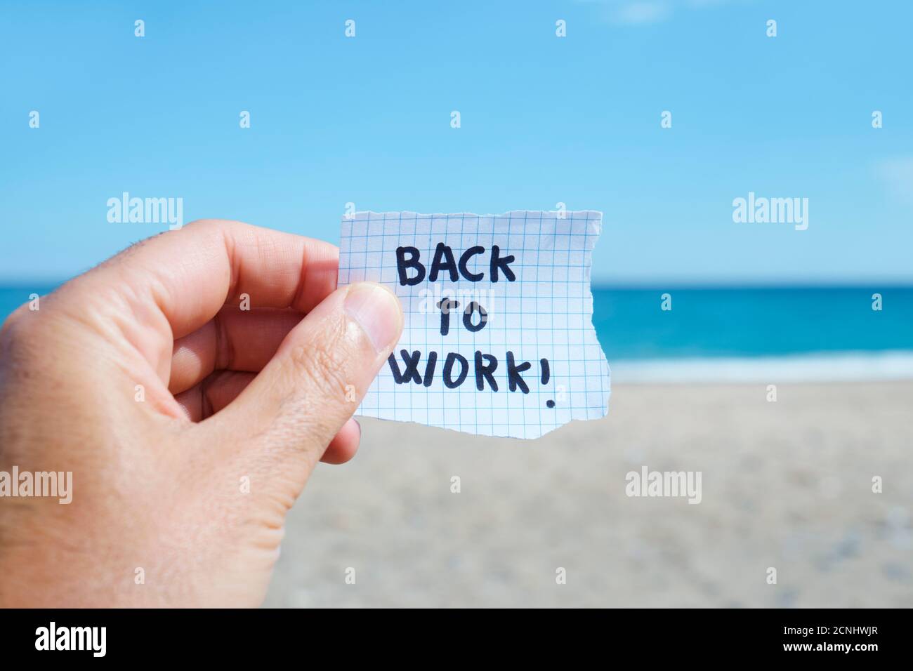 Nahaufnahme der Hand eines jungen kaukasischen Mannes am Strand, vor dem Ozean, hält ein Stück Papier mit dem Text zurück, um die Arbeit in ihm geschrieben Stockfoto