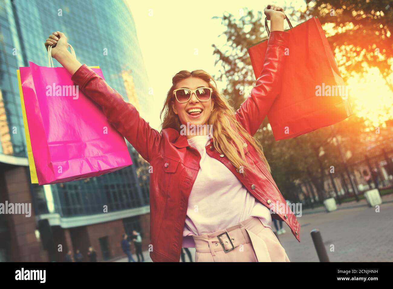 Schönes lächelndes Mädchen in Sonnenbrille hält Einkaufstaschen und genießt ihr Einkaufen. Stockfoto