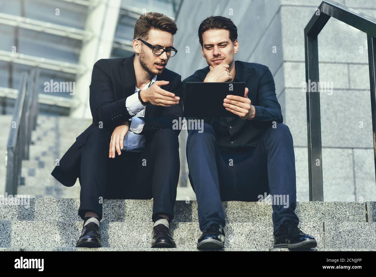 Zwei Geschäftsleute, die auf einer Treppe sitzen und Zeitungen betrachten. Stockfoto