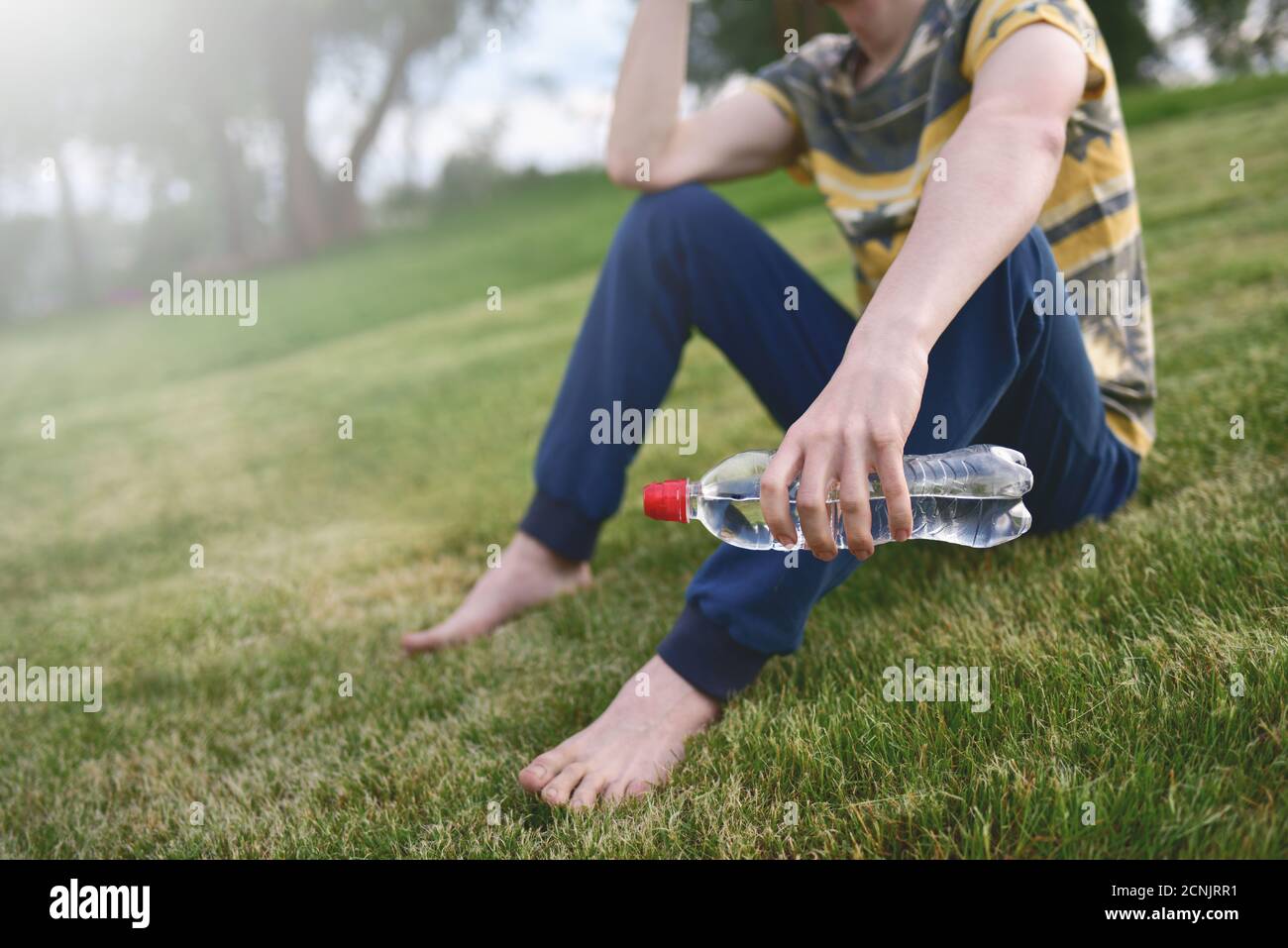 Junge kaukasischen Mann Läufer entspannend hält Trinkwasser Flasche und Sitzen auf Gras im Park im Freien nach dem Sport an Früh Stockfoto