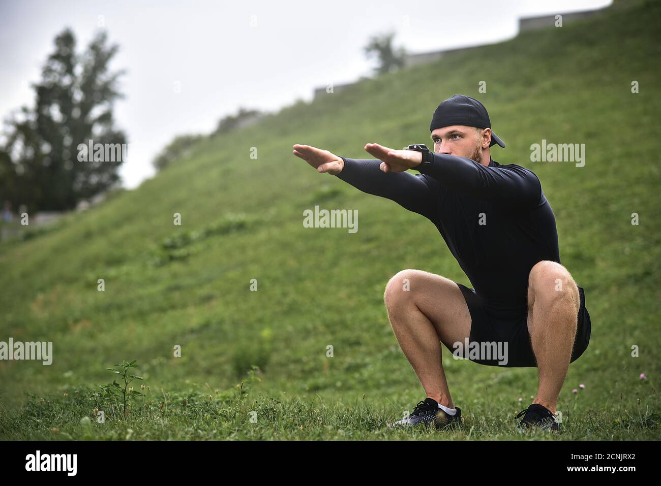 Junge kaukasische Mann Durchführung Kniebeugen vor Joggen auf dem Fußweg im Park. Stockfoto