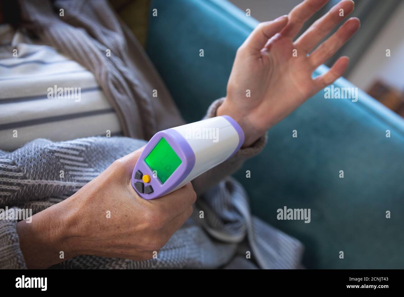 Mittlerer Abschnitt der kranken kaukasischen Frau, die Zeit zu Hause verbringt, soziale Distanzierung und Selbstisolierung in Quarantäne-Sperre, sitzend auf Sofa in bla eingewickelt Stockfoto