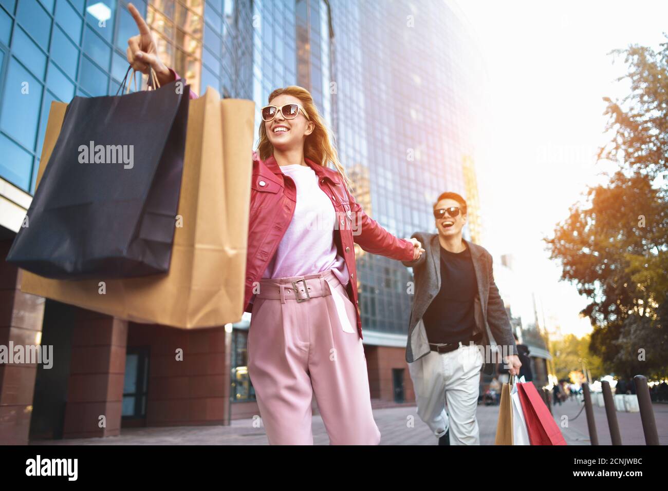 Vorderansicht eines lässigen Einkaufsbummers, der auf der Straße in Richtung Kamera läuft und bunte Einkaufstaschen hält. Stockfoto