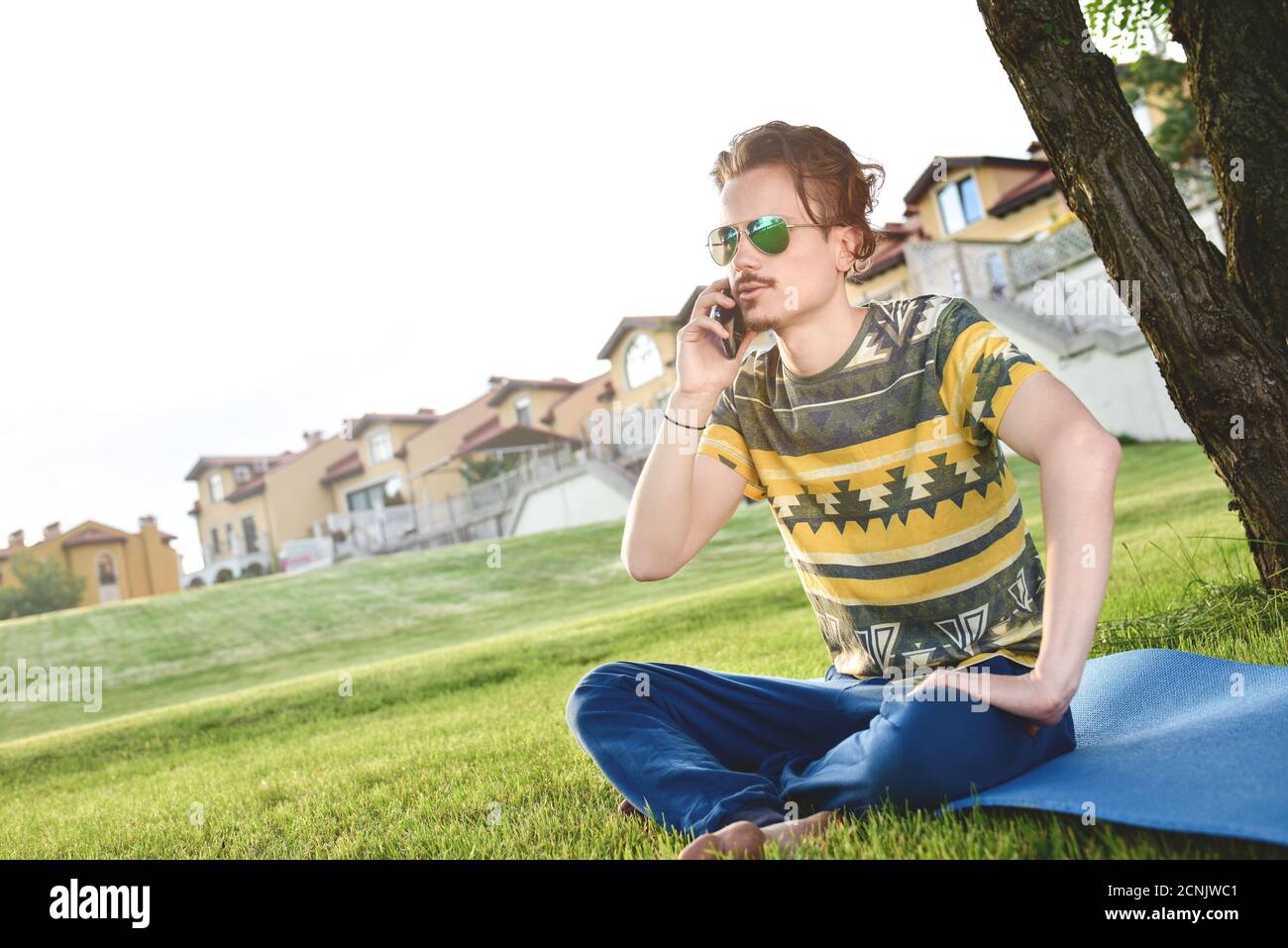 Junge stilvolle gutaussehende Mann sitzt auf Gras und sprechen auf dem Telefon ruhen im Park. Eine Pause einlegen Stockfoto