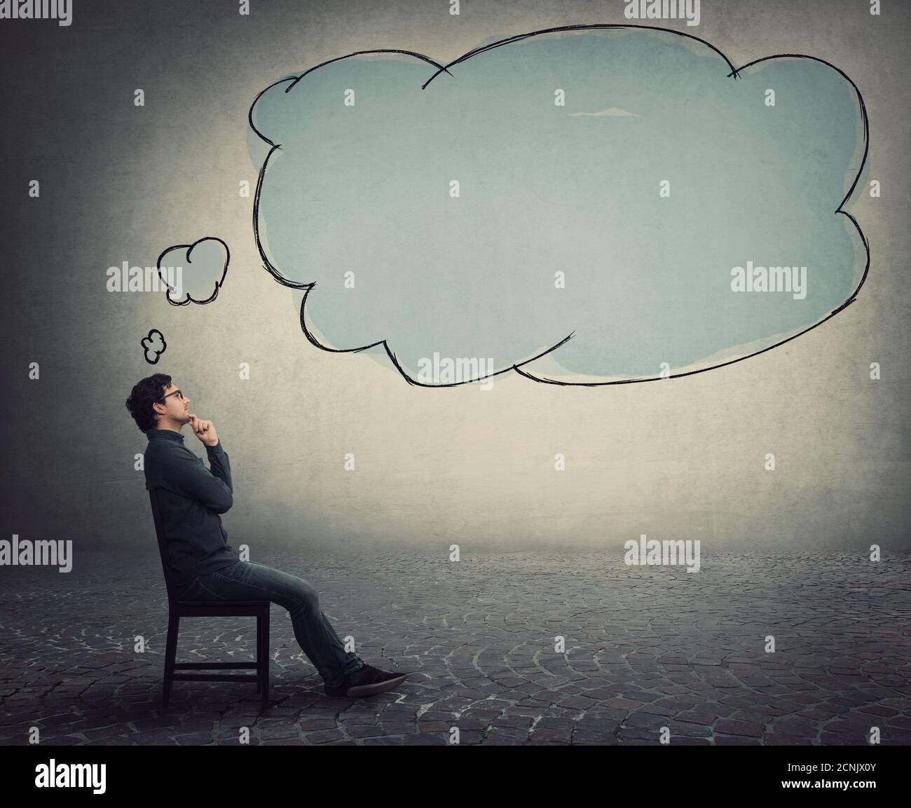 Seitenansicht Geschäftsmann sitzt auf einem Stuhl, hält die Hand unter dem Kinn, nachdenkliche Geste, und eine leere Gedankenblase, Denkwolke, kommt aus seinem Kopf. Stockfoto