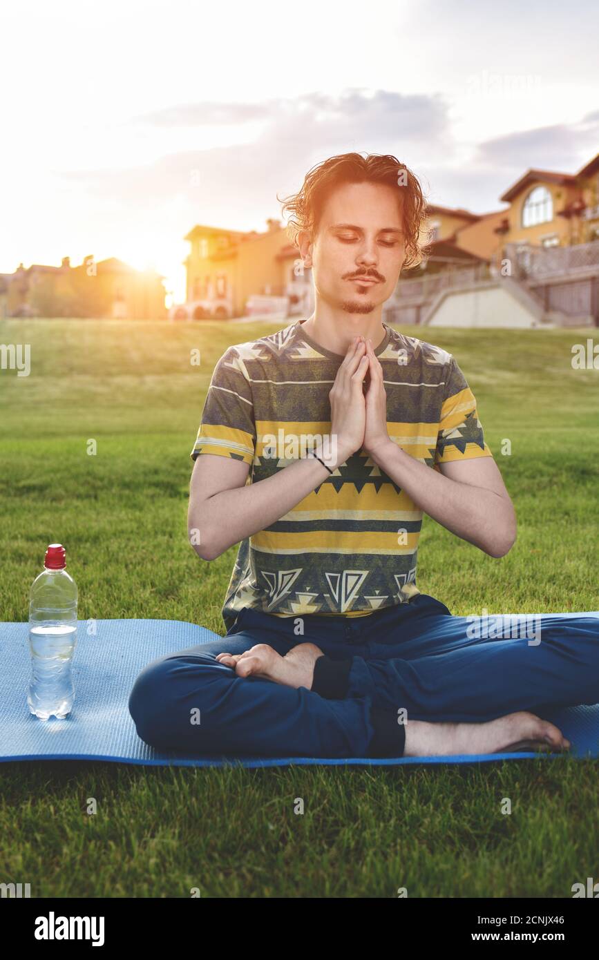 Junger Mann meditiert im Park, sitzt mit geschlossenen Augen und seinen Händen zusammen.Natur genießen, Yoga und Meditation Stockfoto