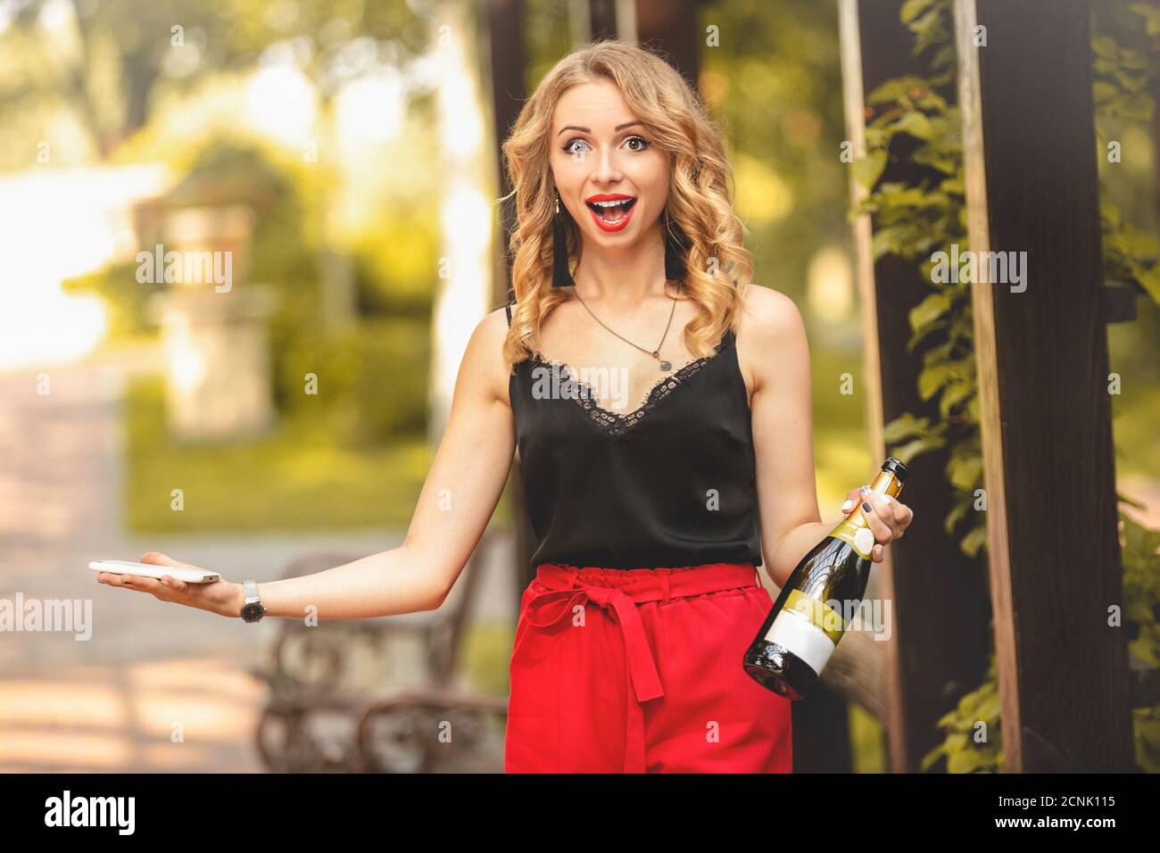 Glückliche junge attraktive kaukasische Frau Student lachen freudig, am Telefon zu sprechen, hält eine Flasche Champagner und Callin Stockfoto