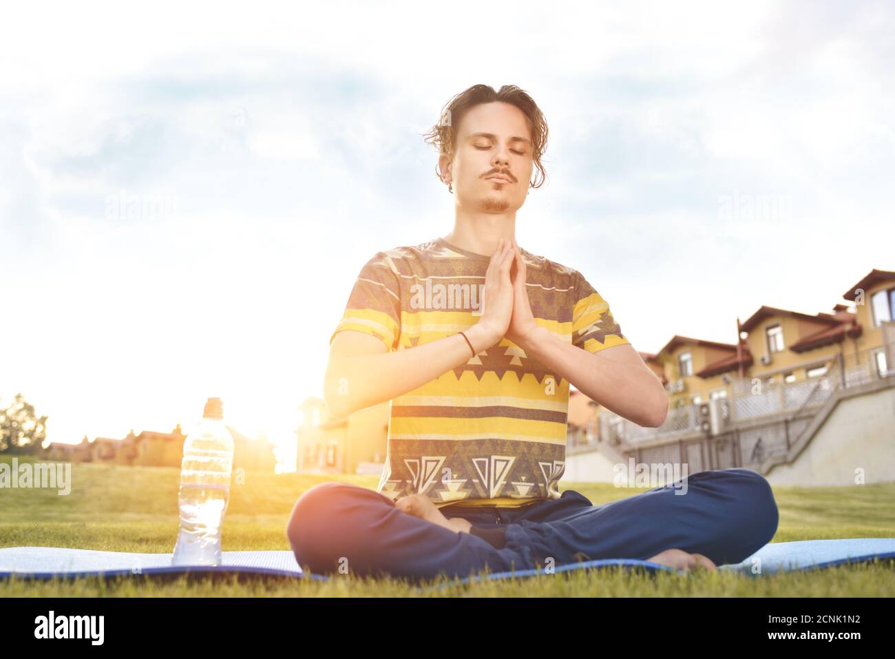 Junger Mann meditiert im Park, sitzt mit geschlossenen Augen und seinen Händen zusammen.Natur genießen, Yoga und Meditation Stockfoto