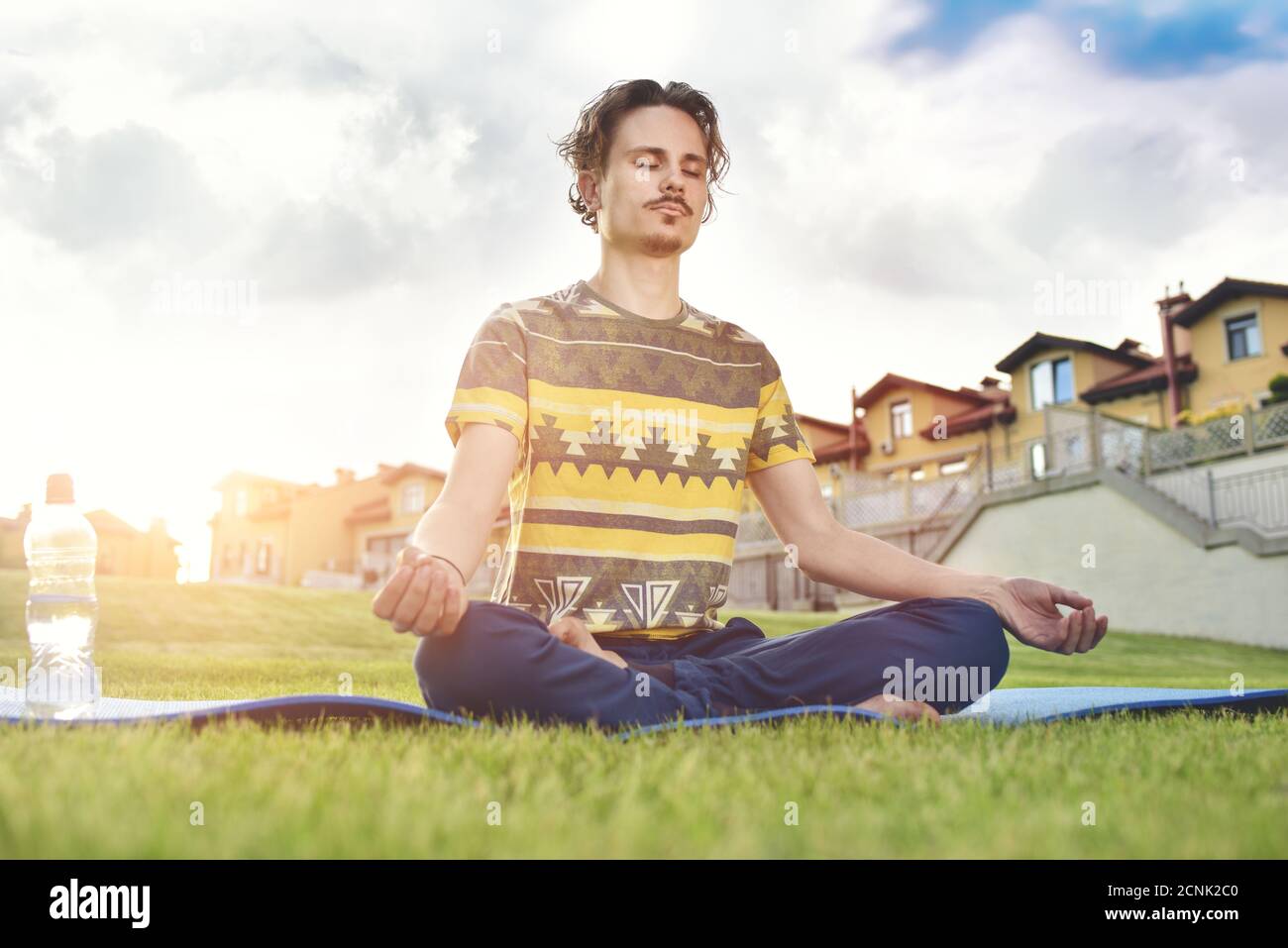 Junger Mann meditiert im Park, sitzt mit geschlossenen Augen und seinen Händen zusammen.Natur genießen, Yoga und Meditation Stockfoto