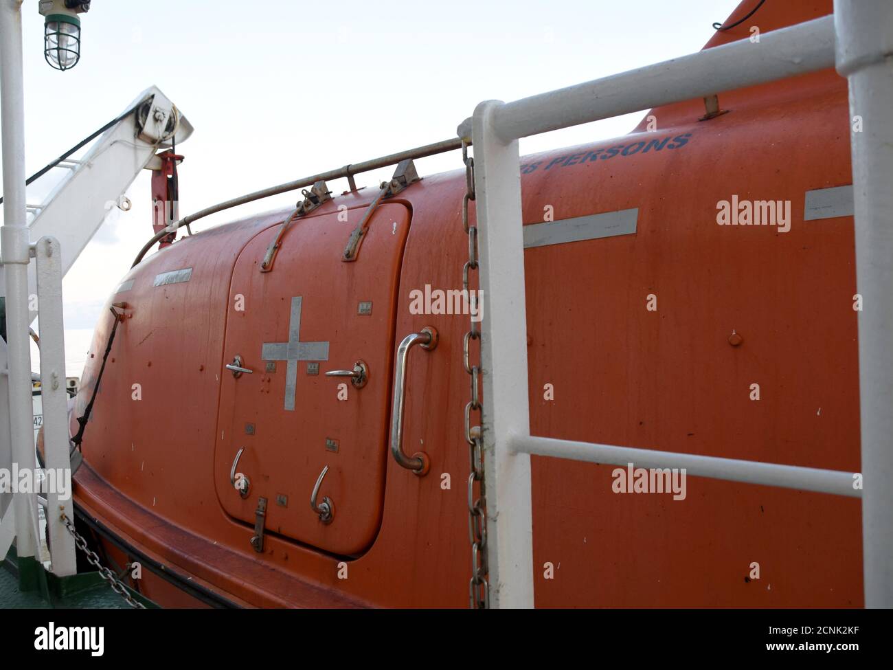 Nahsicht auf das orange Polyurethan Farbe Life Boot mit reflektierenden Klebeband Aufkleber mit Davits und Sicherheitshaken auf dem Handelsfrachtschiff gesichert. Stockfoto