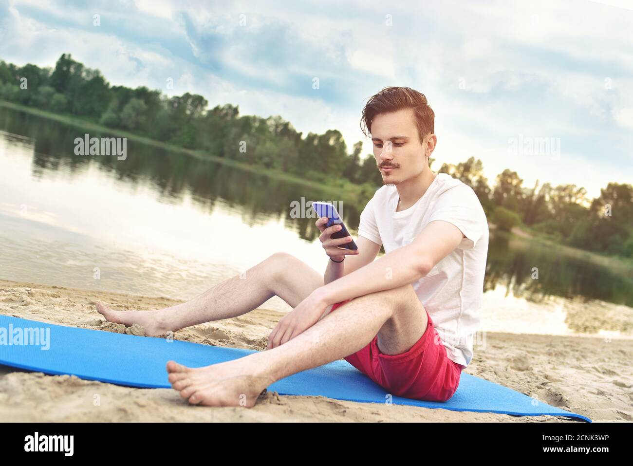 Mann sitzt am Strand am See und schreibt eine sms am Telefon. Stockfoto