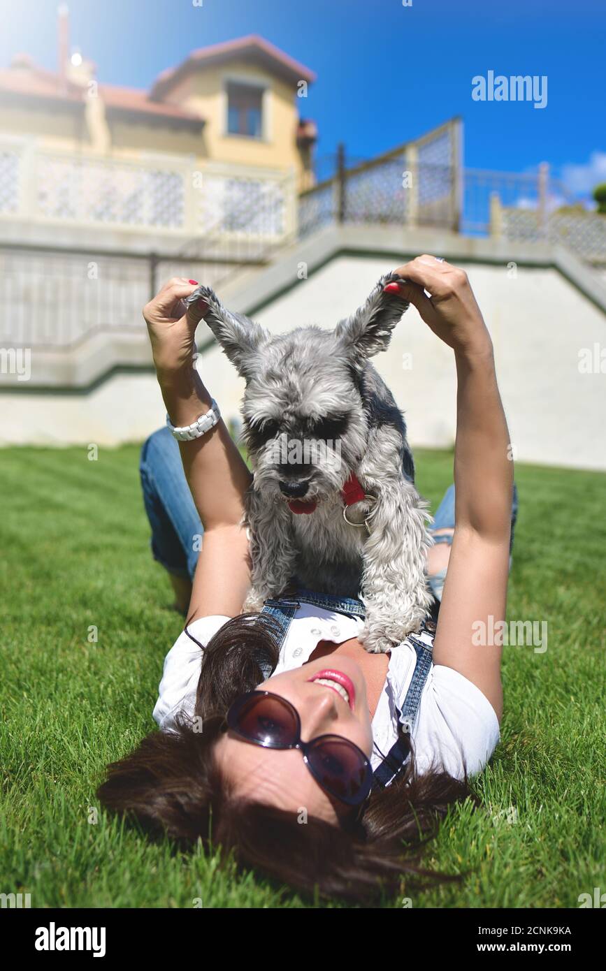 Hübsche Erwachsene kaukasische glückliche Frau, die sich an einem sonnigen Tag mit ihrem geliebten Hund im Park ausruhte. Weibchen liegt auf dem Gras, lächelnd an Stockfoto