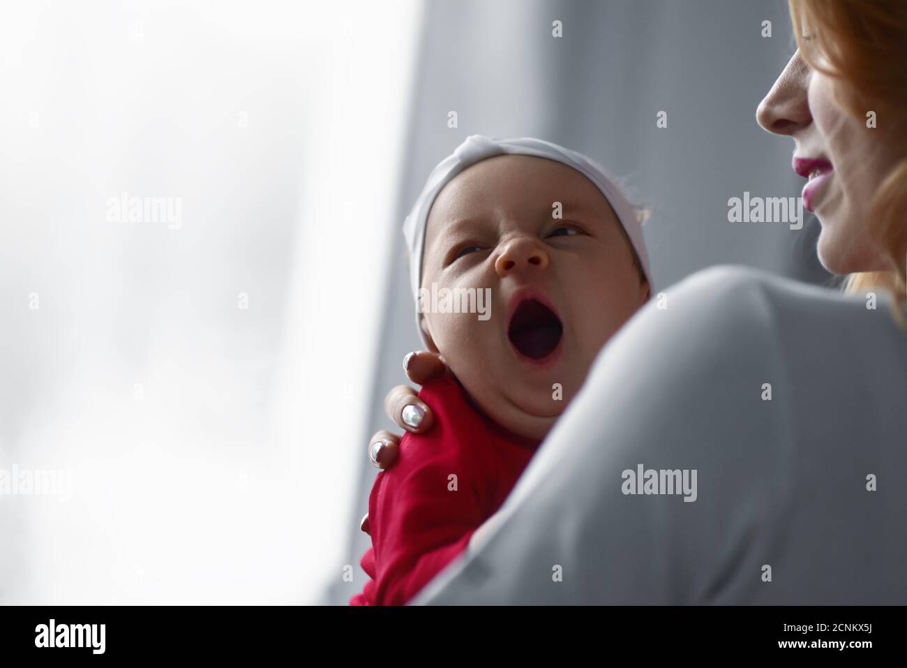 Mutter hält niedlichen neugeborenen Mädchen in ihren Armen. Schläfrig Baby gähnend. Stockfoto