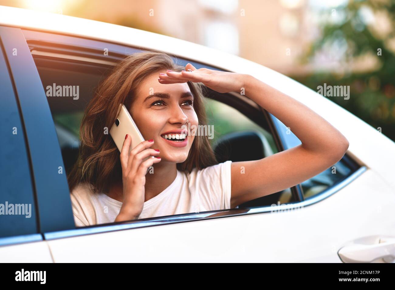 Attraktive Frau mit Telefon im Auto, sonniger Tag Stockfoto