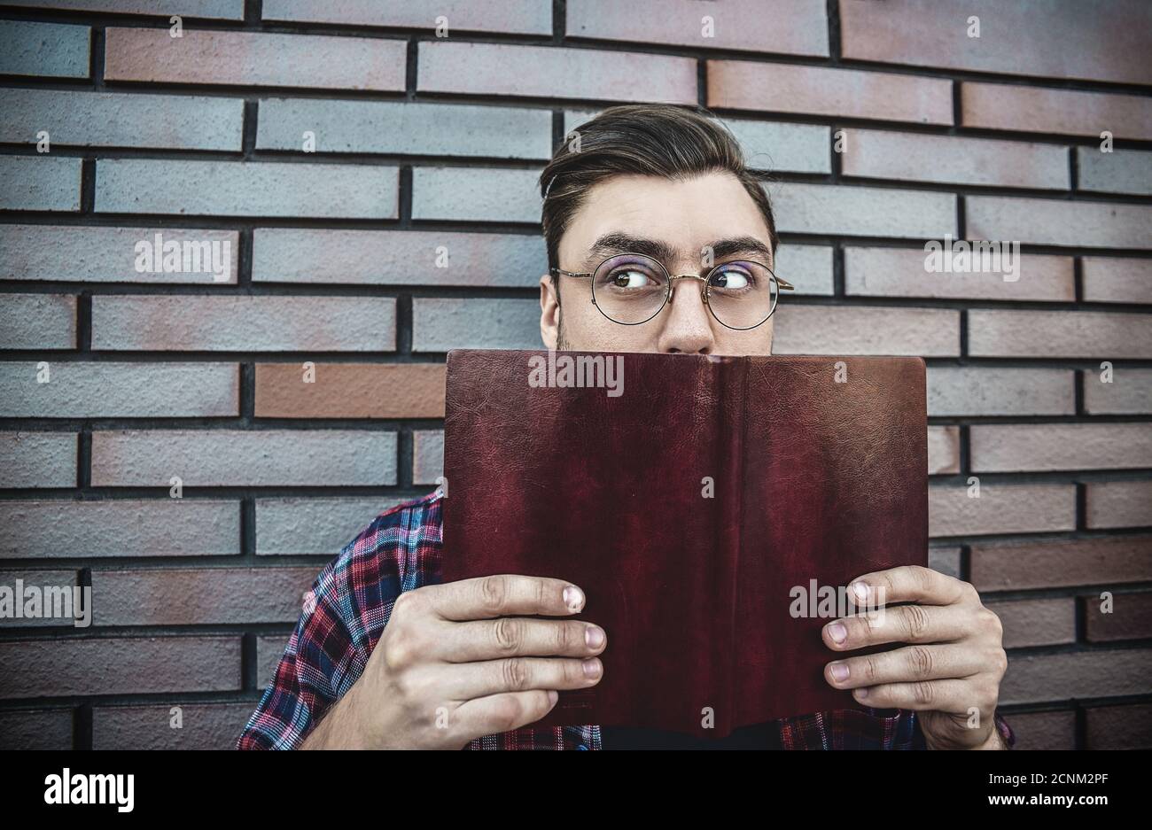 Junge Hipster Kerl trägt Brillen Lesen eines Buches oder Notizbuch auf Backstein Wand Hintergrund. Stockfoto
