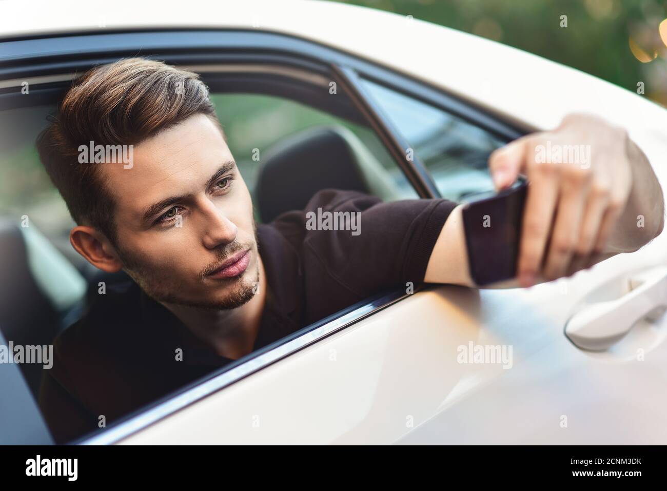 Schöner Mann auf dem Rücksitz des Autos sitzen und ein Telefon verwenden. Stockfoto