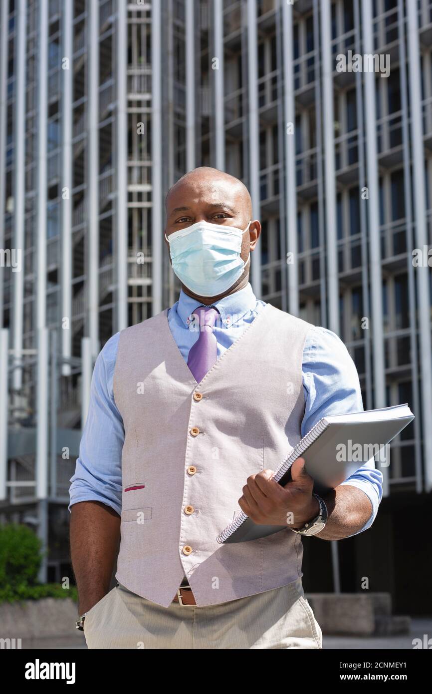 Porträt eines schwarzen Arbeiters mit einem Notizbuch in der Hand. Er trägt eine Gesichtsmaske und formelle Kleidung. Business und neues normales Konzept. Stockfoto