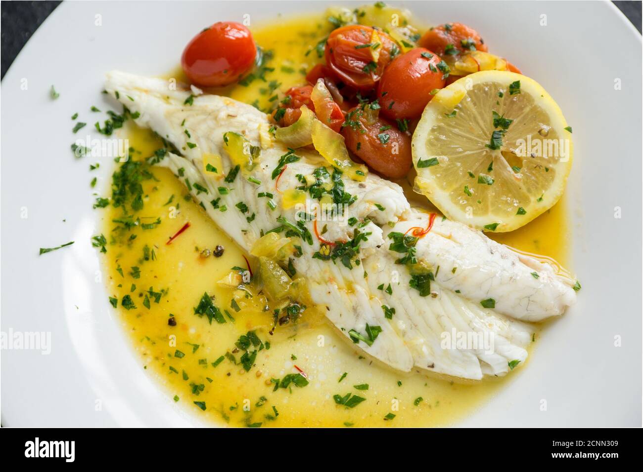 Ein Filet aus einem Brill, Scophthalmus rhombus, das in Olivenöl mit Zwiebeln, Tomaten und Kräutern geröstet wurde. Dorset England GB Stockfoto