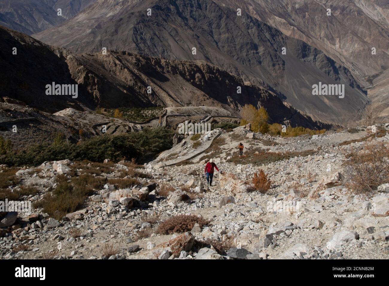 Fotograf und Model wandern an einem klaren Tag zu einem Hügel mit dem sichtbaren Mond, Nako Village, einem See, gelben Bäumen und strukturierten Bergen. Stockfoto